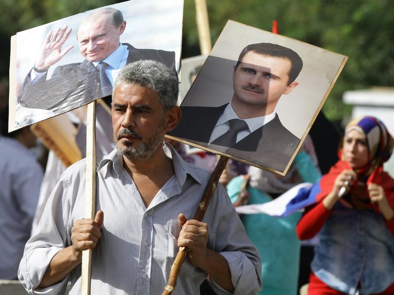 A Syrian man holding portraits of President Bashar Assad and Russian leader Vladimir Putin joins several hundred pro-government demonstrators near the Russian embassy in Damascus on Tuesday to express support for Moscow's air war in Syria. Two rockets later struck the embassy compound and sparked panic among the crowd. No one was killed.