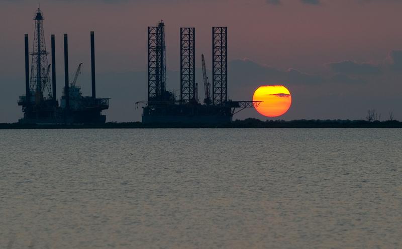 The sun sets behind two under-construction offshore oil platform rigs in Port Fourchon, La, June 14, 2010, as cleanup of the BP Deepwater Horizon oil continues.
