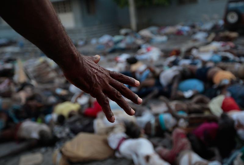 A man points to the hundreds of bodies piled up outside the morgue and main hospital on January 15, 2010 in Port-au-Prince, Haiti.