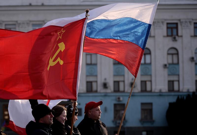 Men hold Russian (R) and Soviet Union flags in Simferopol's Lenin Square on March 16, 2014. Polls opened yesterday for a referendum on the peninsula of Crimea.