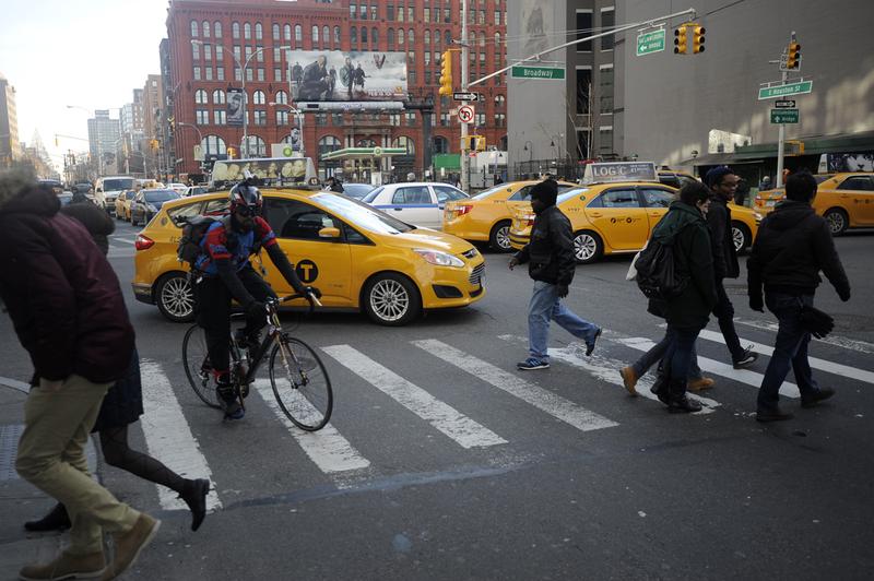 A car turns right in Manhattan as pedestrians cross the street.