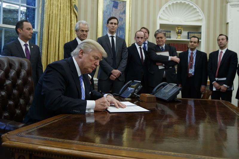 President Donald Trump signs an executive order implementing a federal government hiring freeze, Monday, Jan. 23, 2017, in the Oval Office of the White House in Washington. 