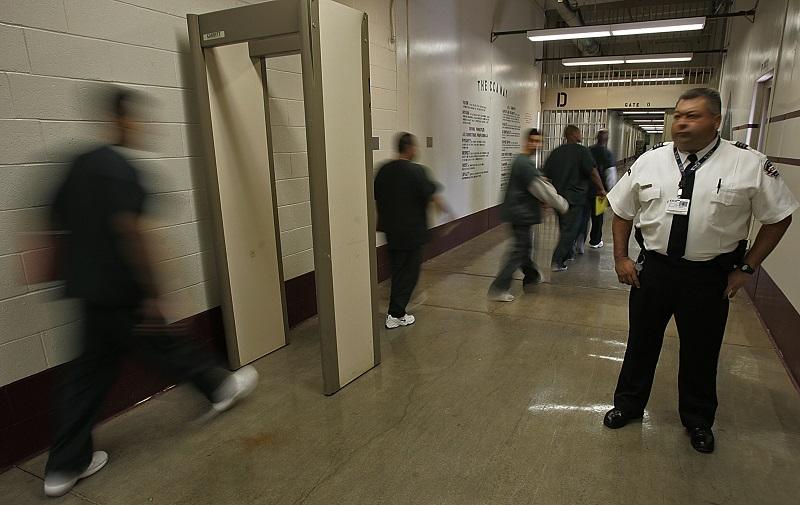 Inmates from California pass through a metal detector under the watchful eye of a guard at the Florence Correctional Center, a prison operated by Corrections Corporation of America in Florence, Ariz.