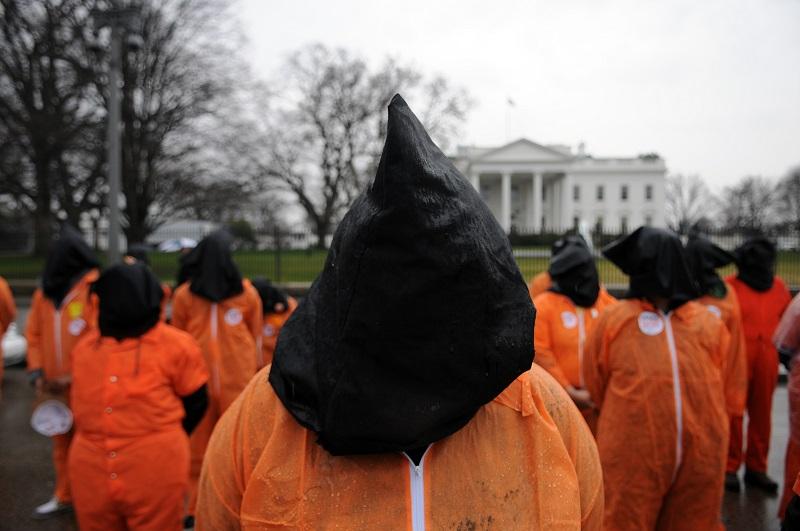 Members of the organization Witness Against Torture wear orange prison jump suits with handcuffs and a hood over their heads during a demonstration urging the government to close down the facility.