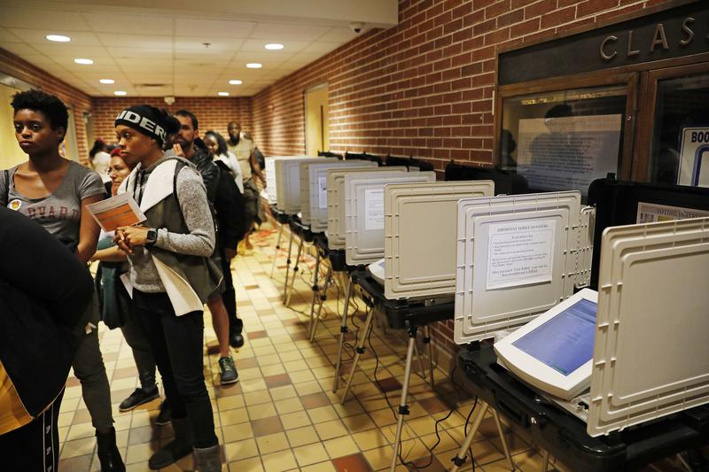 Voters wait in line on election day next to unused machines as the precinct switched over to paper ballots after a judge ordered the polling location to remain open until 10 p.m., a full three hours a