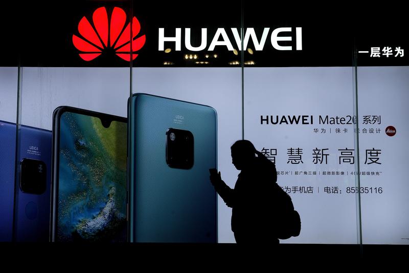 A woman browses her smartphone as she walks by a Huawei store at a shopping mall in Beijing, Tuesday, Dec. 11, 2018.