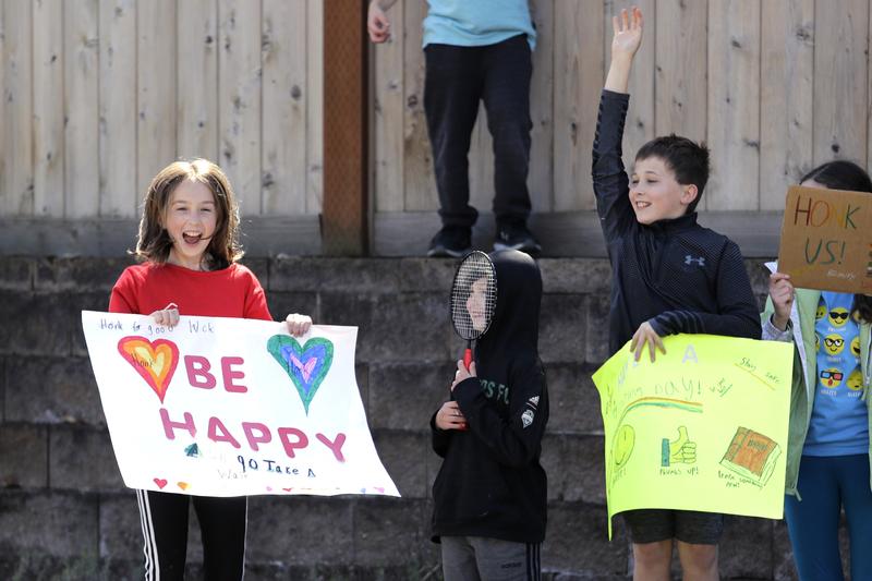 Linnea Egan-Stark, 13, left, cheers with her brothers Leo, 8, and Lucas, 10, and friend Mia Skiena, 13, right, after getting a passing driver to honk their horn in response to their signs.