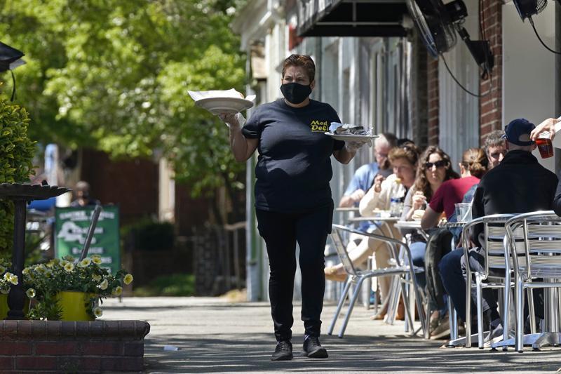 A member of the wait staff delivers food to outdoor diners along the sidewalk at the Mediterranean Deli restaurant in Chapel Hill, N.C., Friday, April 16, 2021.