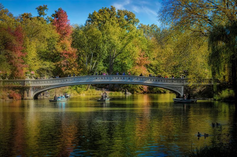 View of the Bow Bridge and boaters on the Lake on a warm fall day in Central Park, Manhattan
