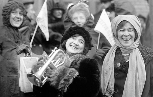 Suffragists rally, February 1913, waving pennants reading Votes for Women.